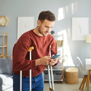 A man using crutches while checking his phone, representing adult disability benefits.
