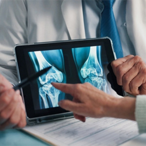 Doctor pointing to a hip X-ray on a tablet during a disability consultation.