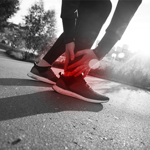 Close-up of a person holding their injured ankle while sitting on the ground.