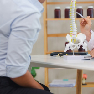 A doctor pointing to a spine model to explain back surgery for a disability claim.