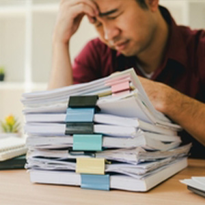 A person looking stressed while reviewing a large stack of tax and benefit documents.