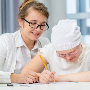 A teacher assisting a young student with a disability in a classroom setting.