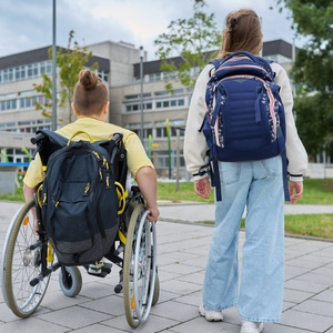 A student in a wheelchair and a walking student heading toward a school building.