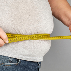 A person measuring their waist with a yellow tape measure for an obesity-related claim.