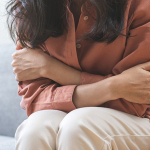 A woman sitting on the floor holding her arms, representing trauma-related distress.