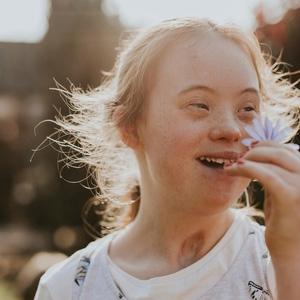 A joyful girl with Down syndrome holding a flower, representing SSDI/SSI benefits.