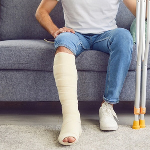 A person with a leg cast and crutches sitting on a sofa, representing injury claims.