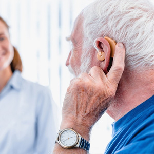 A senior man adjusting his hearing aid during a consultation for disability benefits.