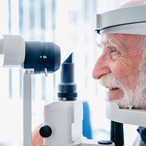 A medical professional using an ophthalmoscope to examine a senior patient's eye.